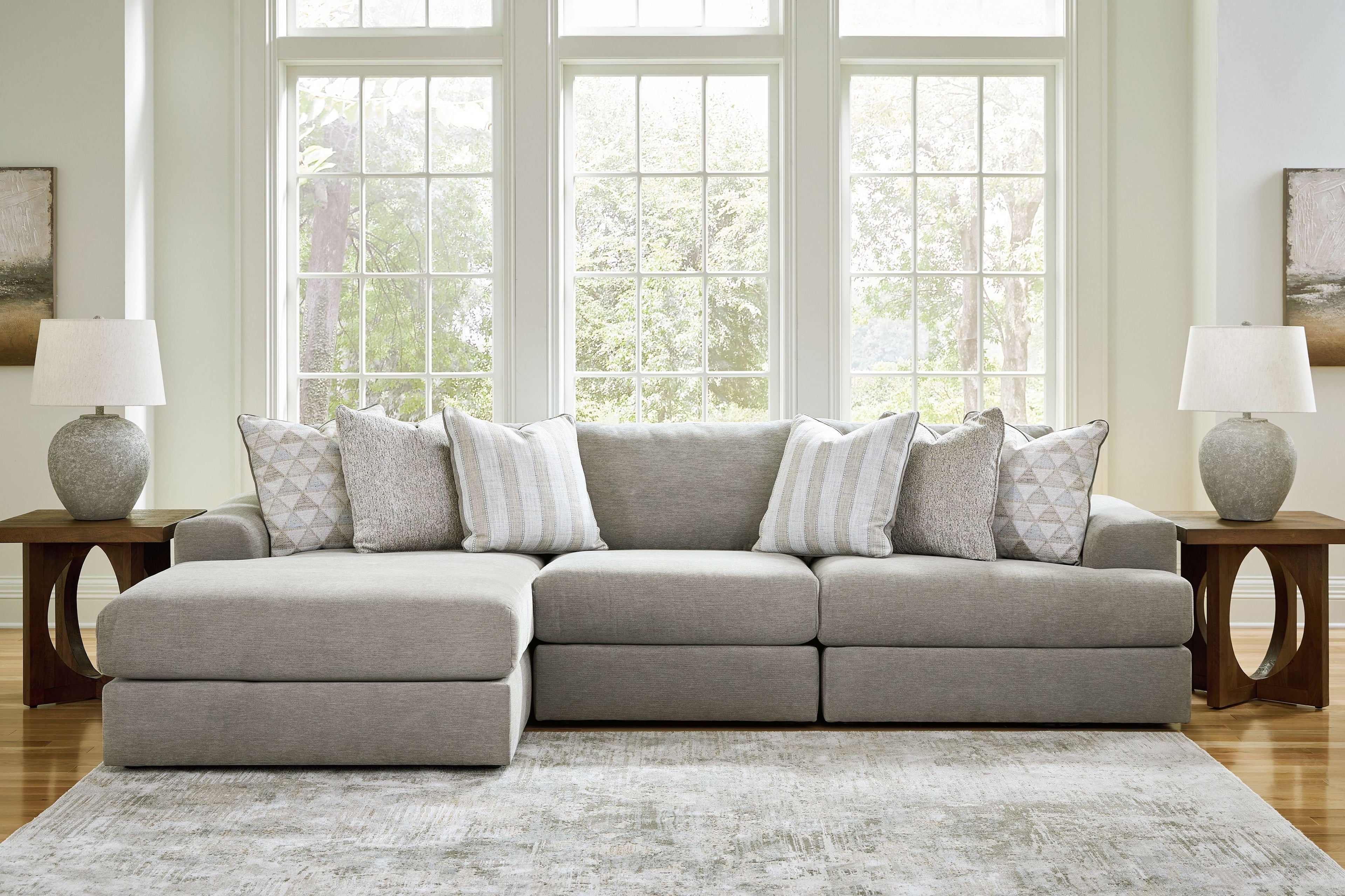 Light gray sectional sofa with corner chaise and multiple patterned throw pillows.
