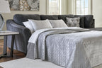 Dark gray sectional sleeper with open mattress, white quilt, and patterned throw pillows