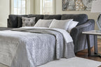 Dark gray sectional sleeper with open bed, white quilt, and accent pillows