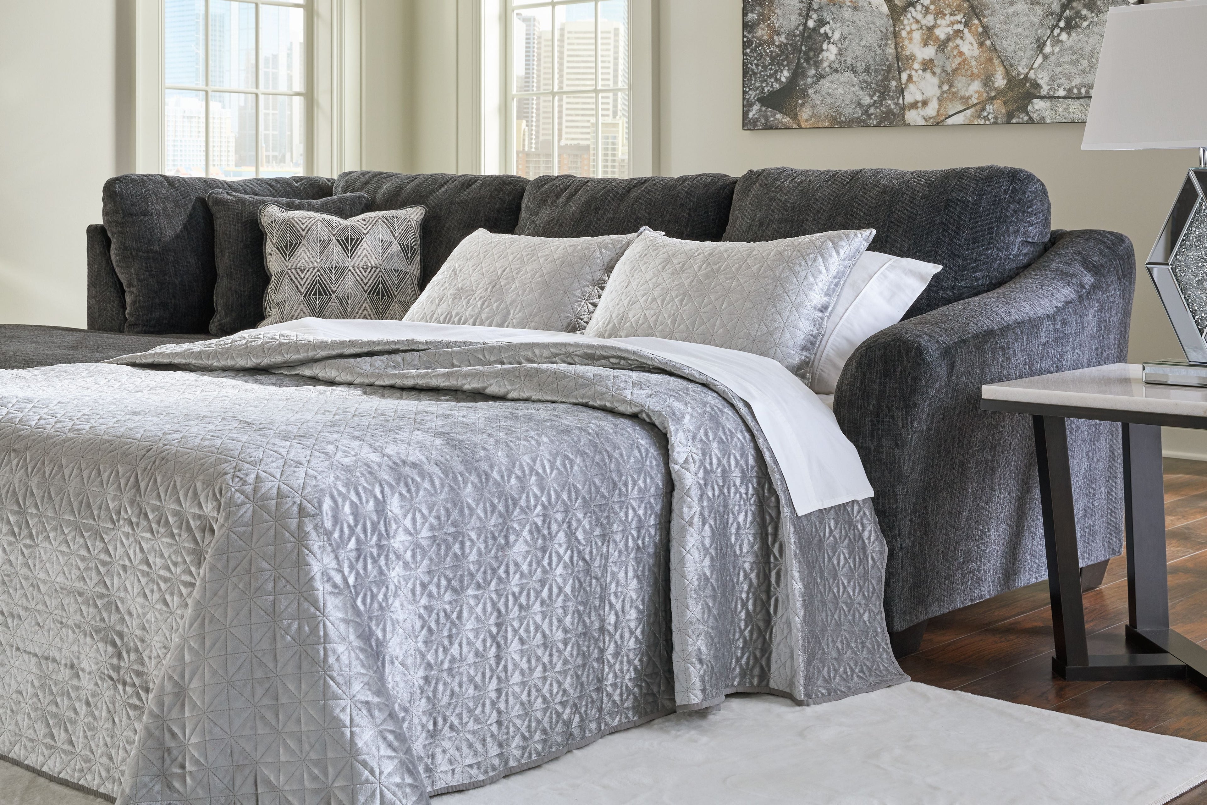 Dark gray sectional sleeper with open bed, white quilt, and accent pillows
