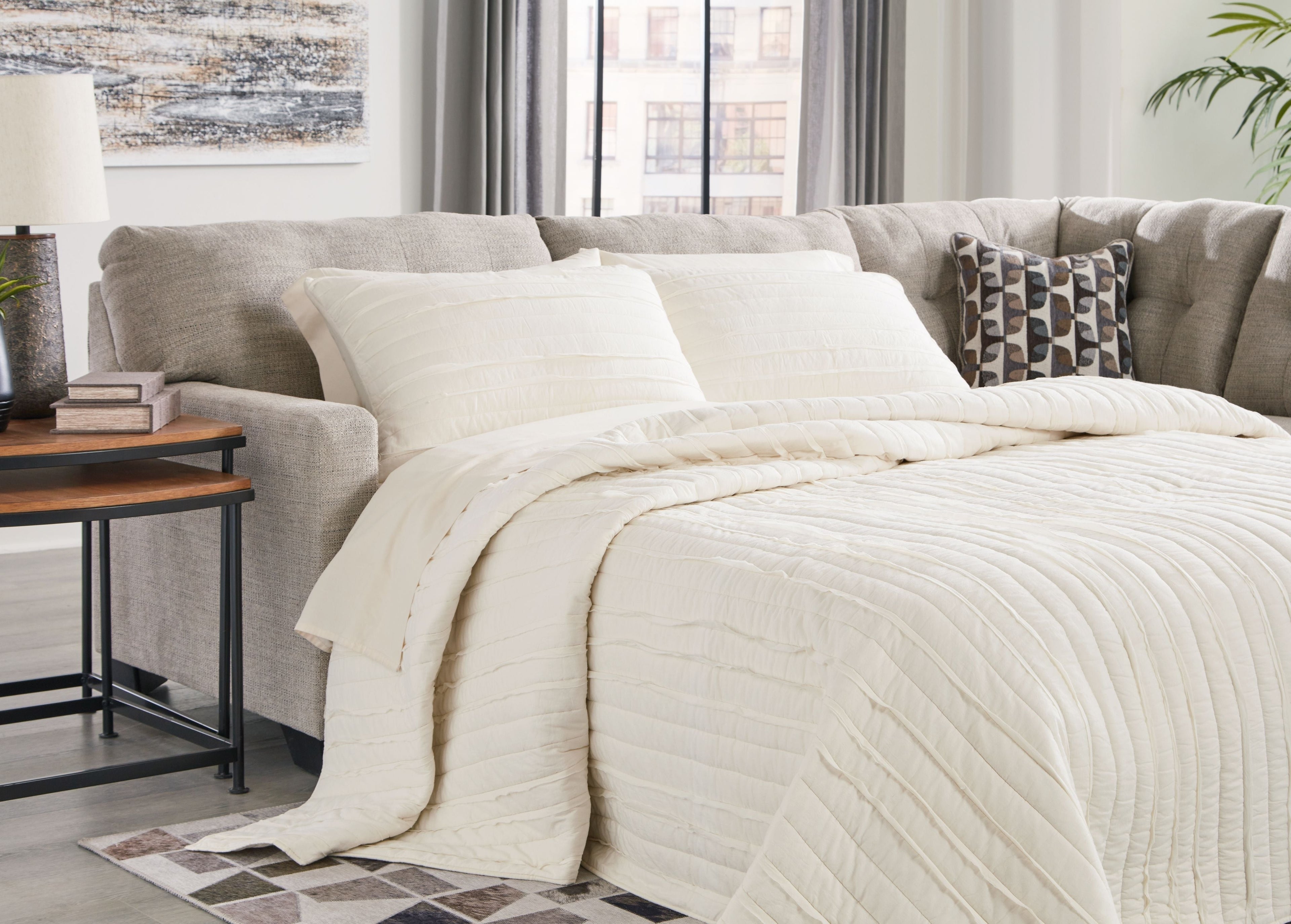 Light gray sectional with chaise, featuring layered white bedding and pillows