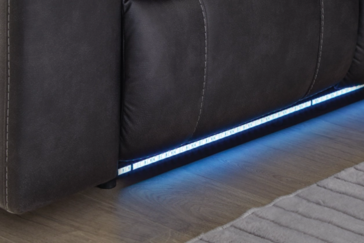 Dark carbon reclining sectional with glowing LED strip along the base and stitched cushions.