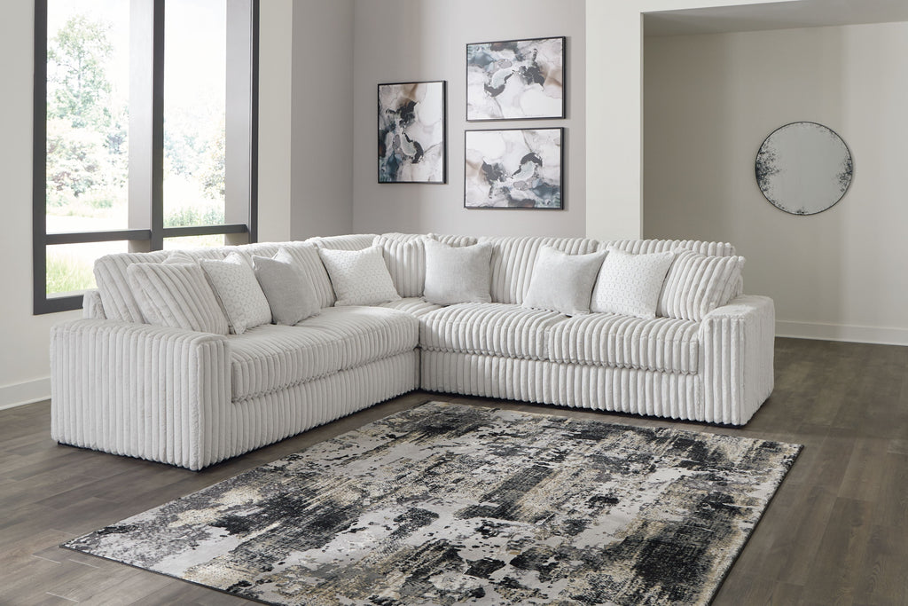 Light gray sectional sofa with corner chaise and stacked back pillows, ribbed upholstery