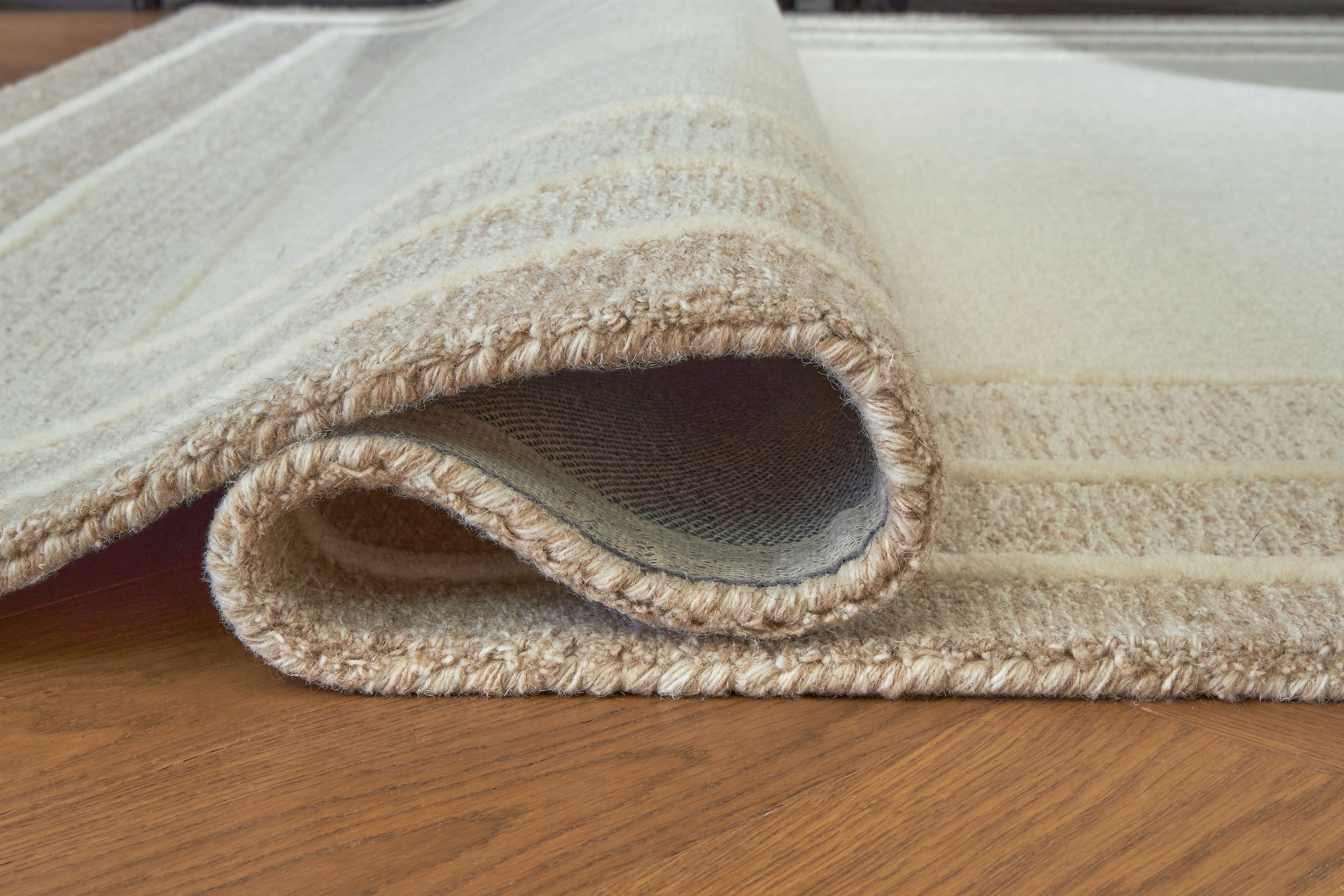 Beige area rug close-up showing rolled edge and thick textured border trim