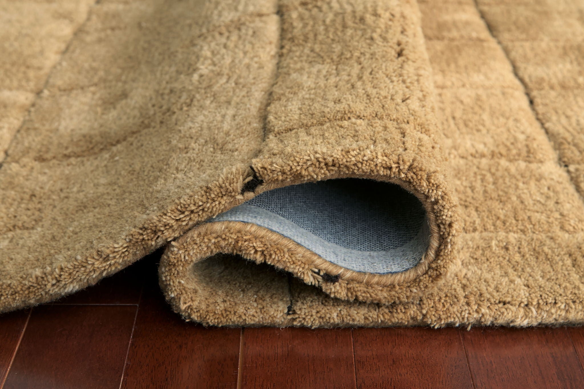 Light brown rug corner with plush pile and curved fabric edge binding