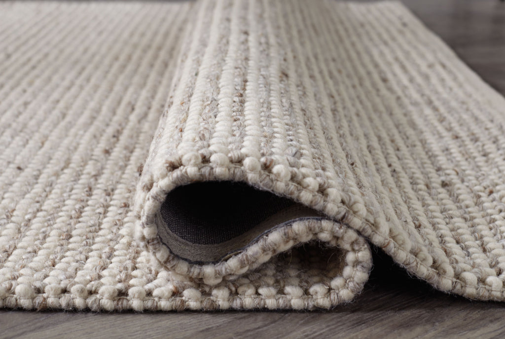 Beige rug corner with rolled edge and visible underside, thick low pile