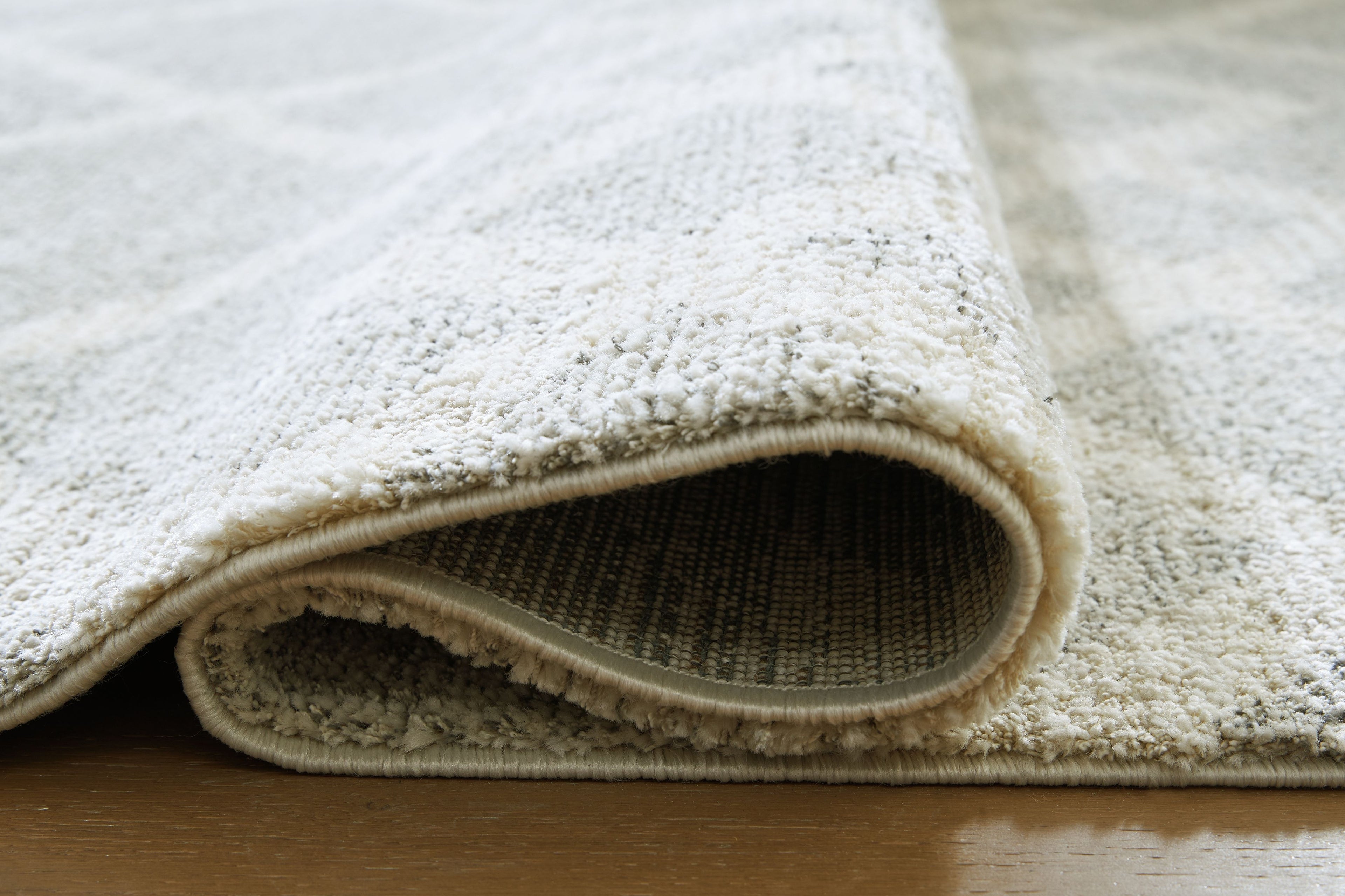 Gray rug corner with short pile texture and tan backing underside