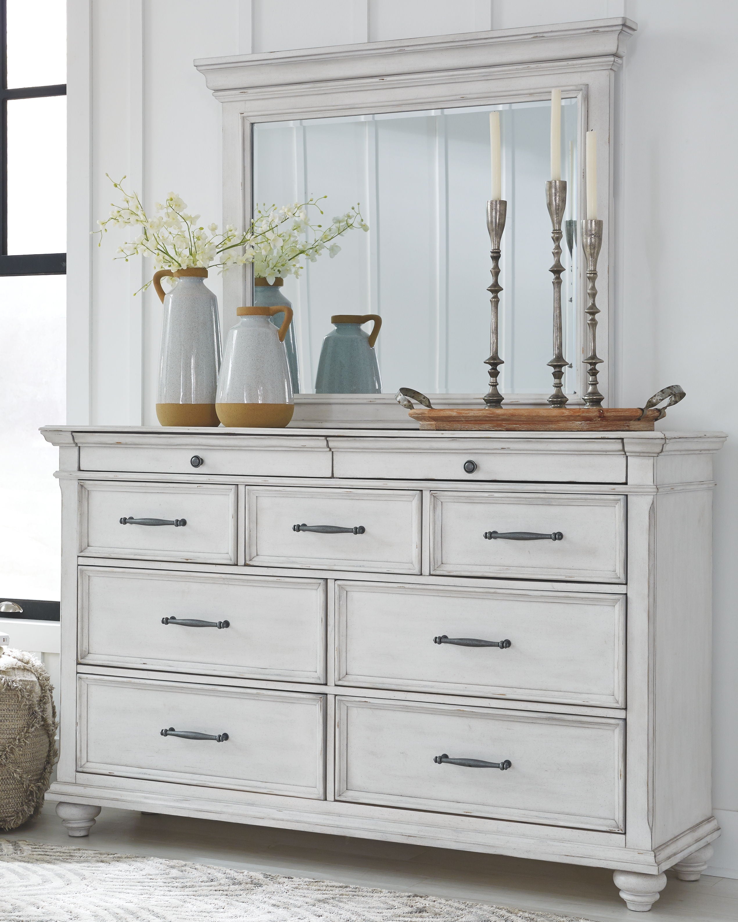 White wood dresser with multiple drawers and a raised top panel, metal bar pulls.