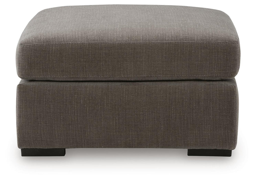 Gray upholstered accent ottoman with thick padded top and front-facing block legs