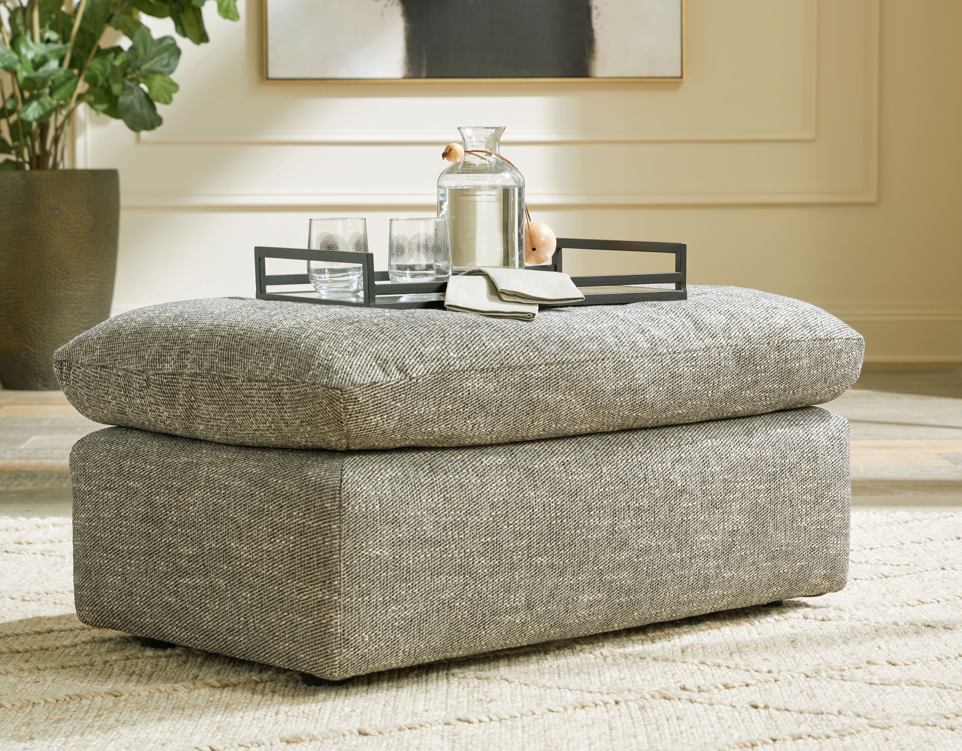 Gray upholstered ottoman with rounded lid and blocky base