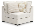 Corner chair in vanilla-beige upholstery with two decorative throw pillows and dark legs