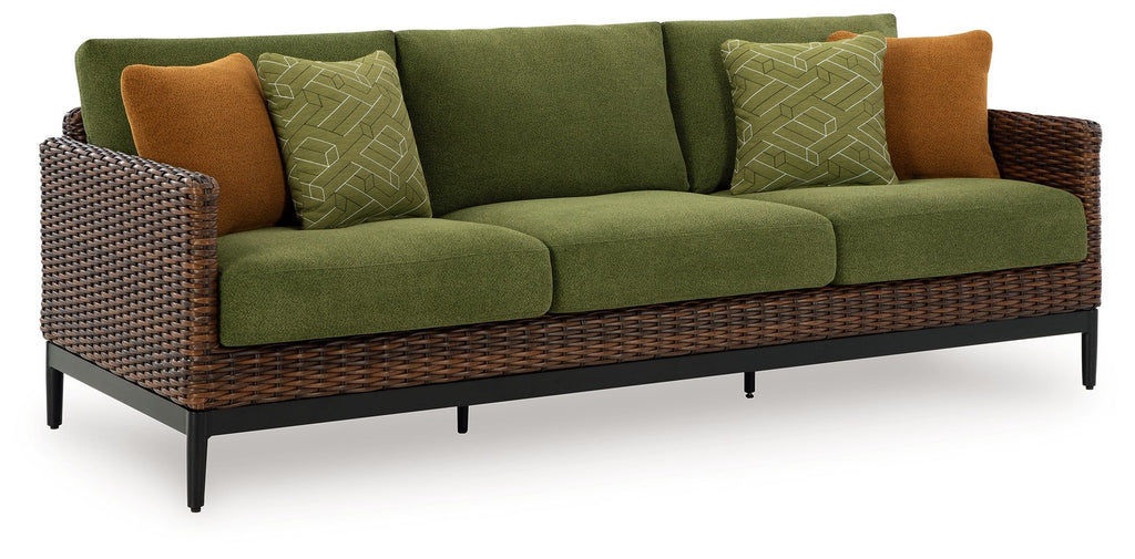 Green sofa with woven wicker sides, brown accent pillows, and patterned green cushions