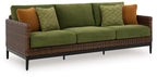 Green sofa with woven wicker sides, brown accent pillows, and patterned green cushions