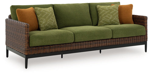Green sofa with woven wicker sides, brown accent pillows, and patterned green cushions