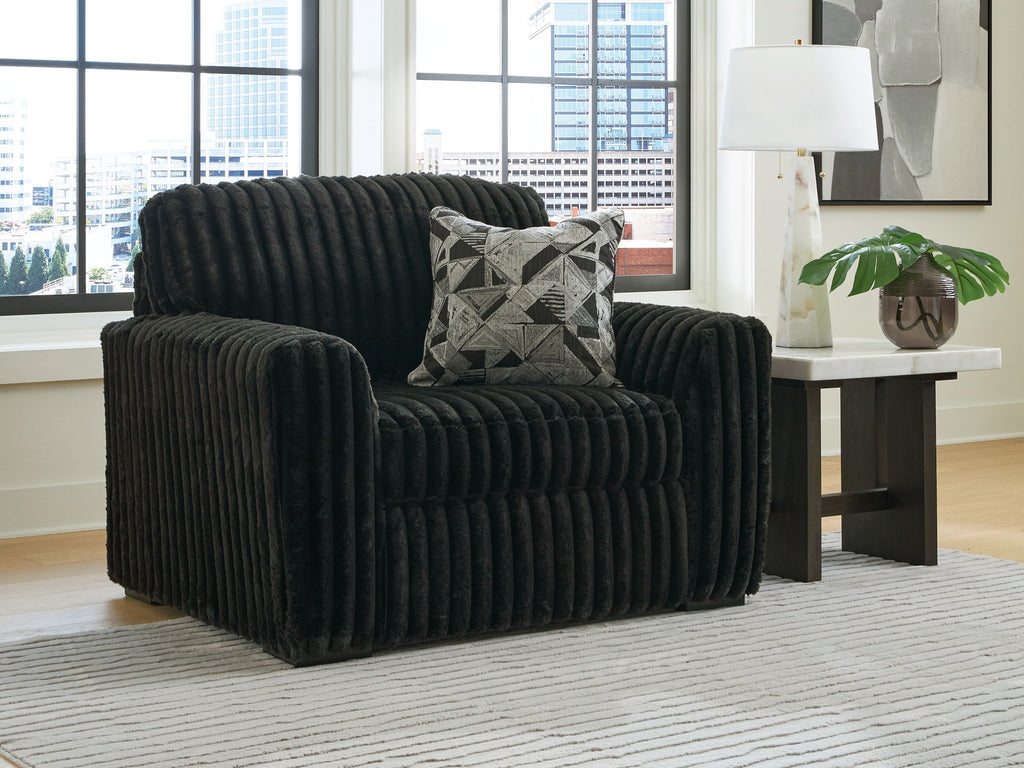 Black chair and a half with patterned pillow, thick ribbed upholstery