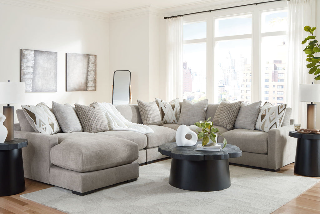 Light gray sectional sofa with chaise seating and patterned cushions beside a side table