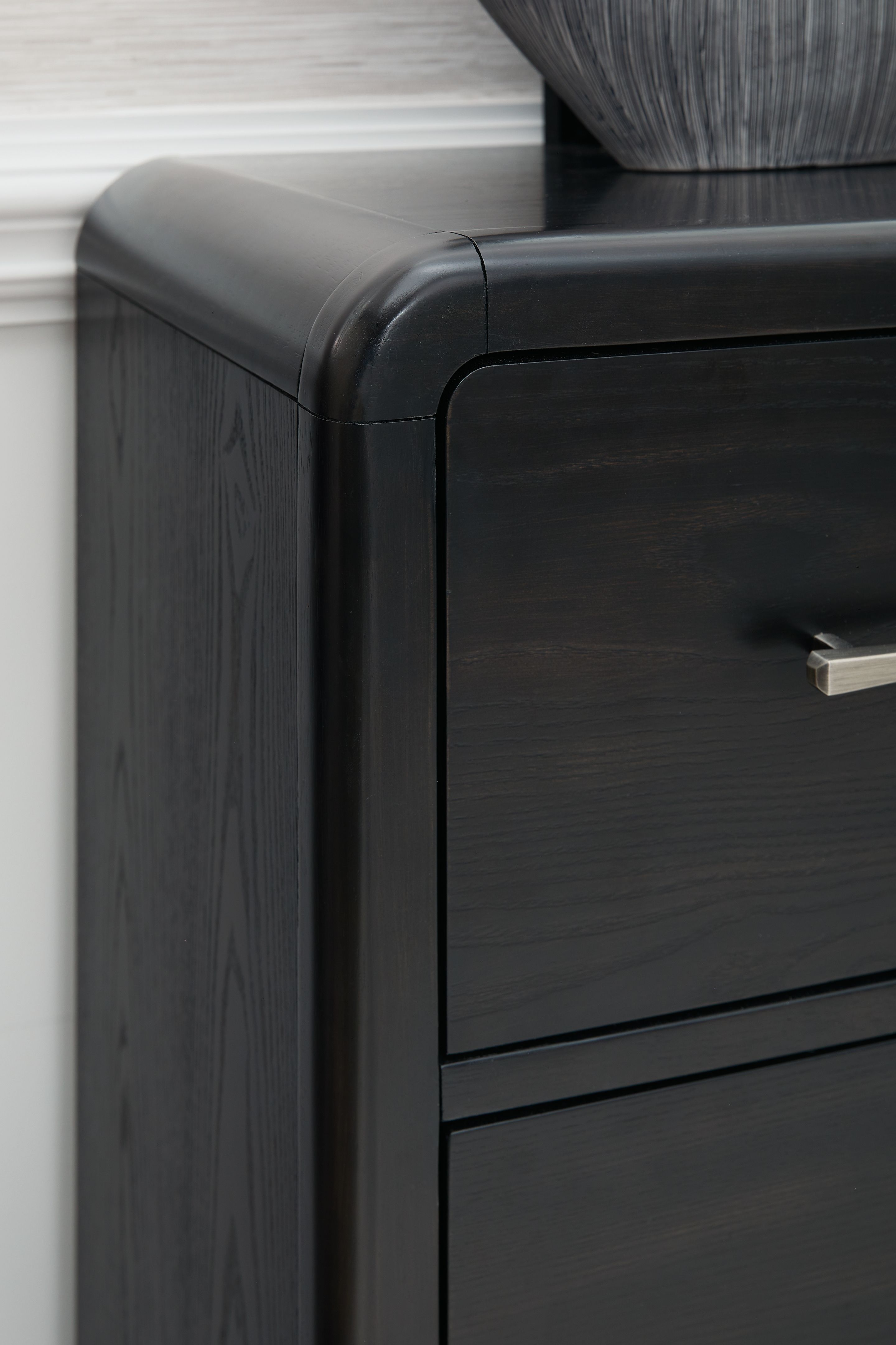 Black dresser corner with curved top edge and metal drawer pull