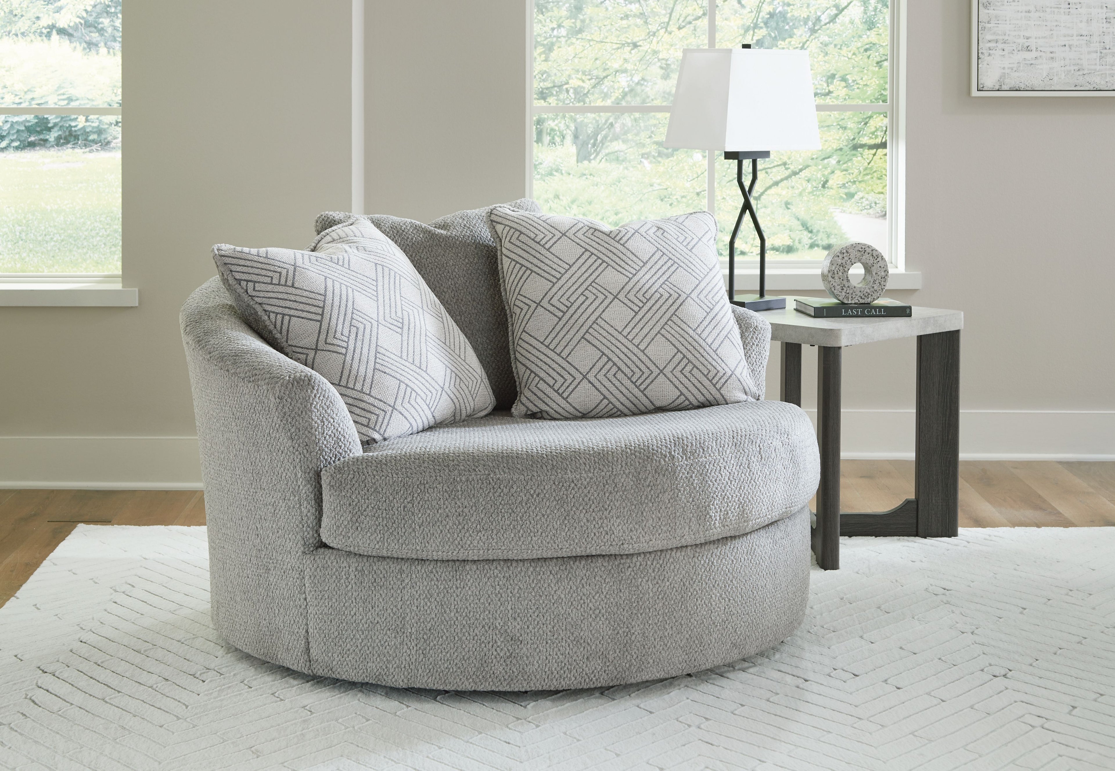 Oversized swivel accent chair in cement gray with patterned throw pillows and wide rounded arms