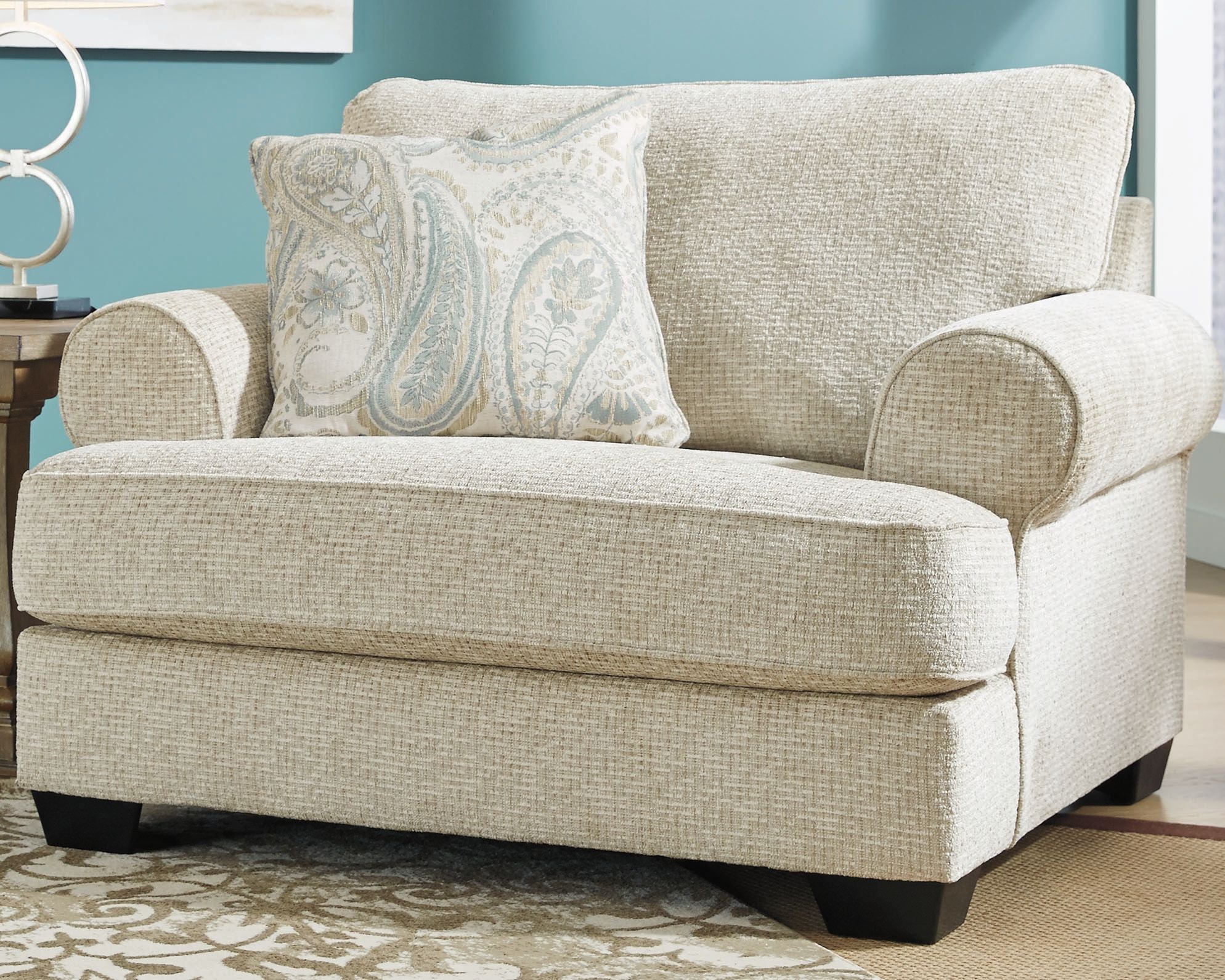 Upholstered armchair with light beige fabric, rolled arms, and blue patterned pillow