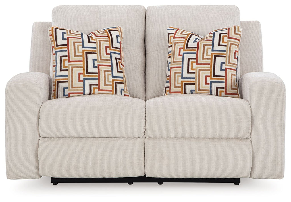 Reclining loveseat with light beige upholstery and two patterned throw pillows
