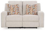 Reclining loveseat with light beige upholstery and two patterned throw pillows