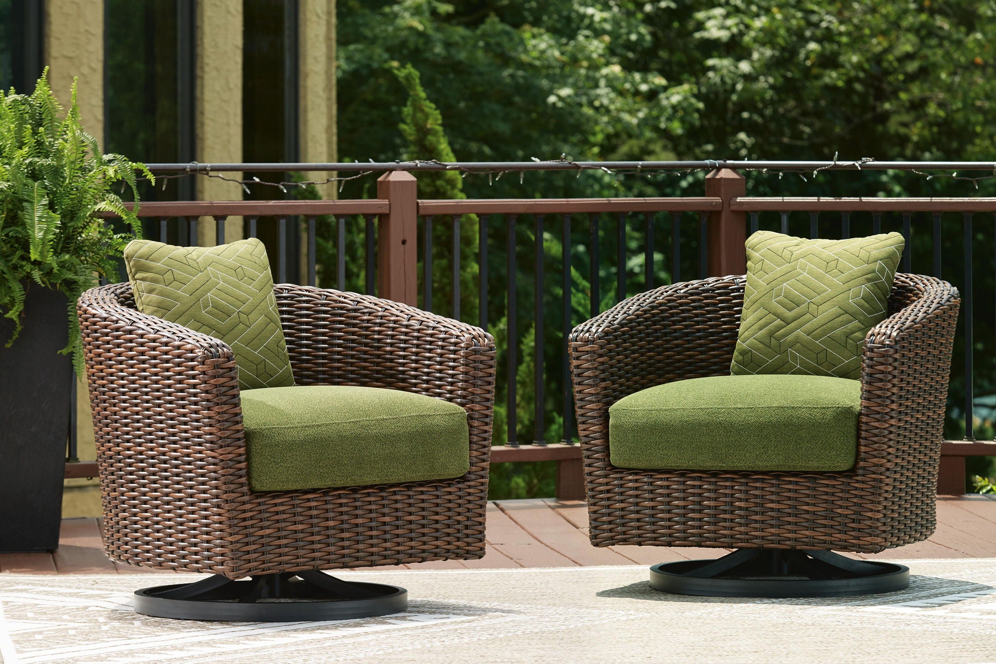 Set of two brown wicker swivel lounge chairs with green cushions and patterned back pillows