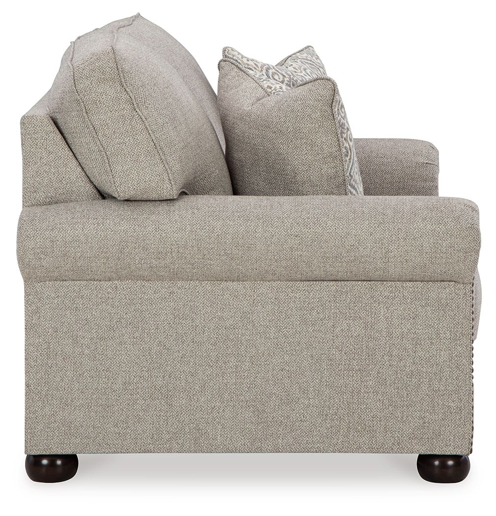 Light gray-beige loveseat from side angle with two patterned accent pillows
