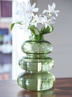 Green glass stacked vase with white blossoms and leafy stems.