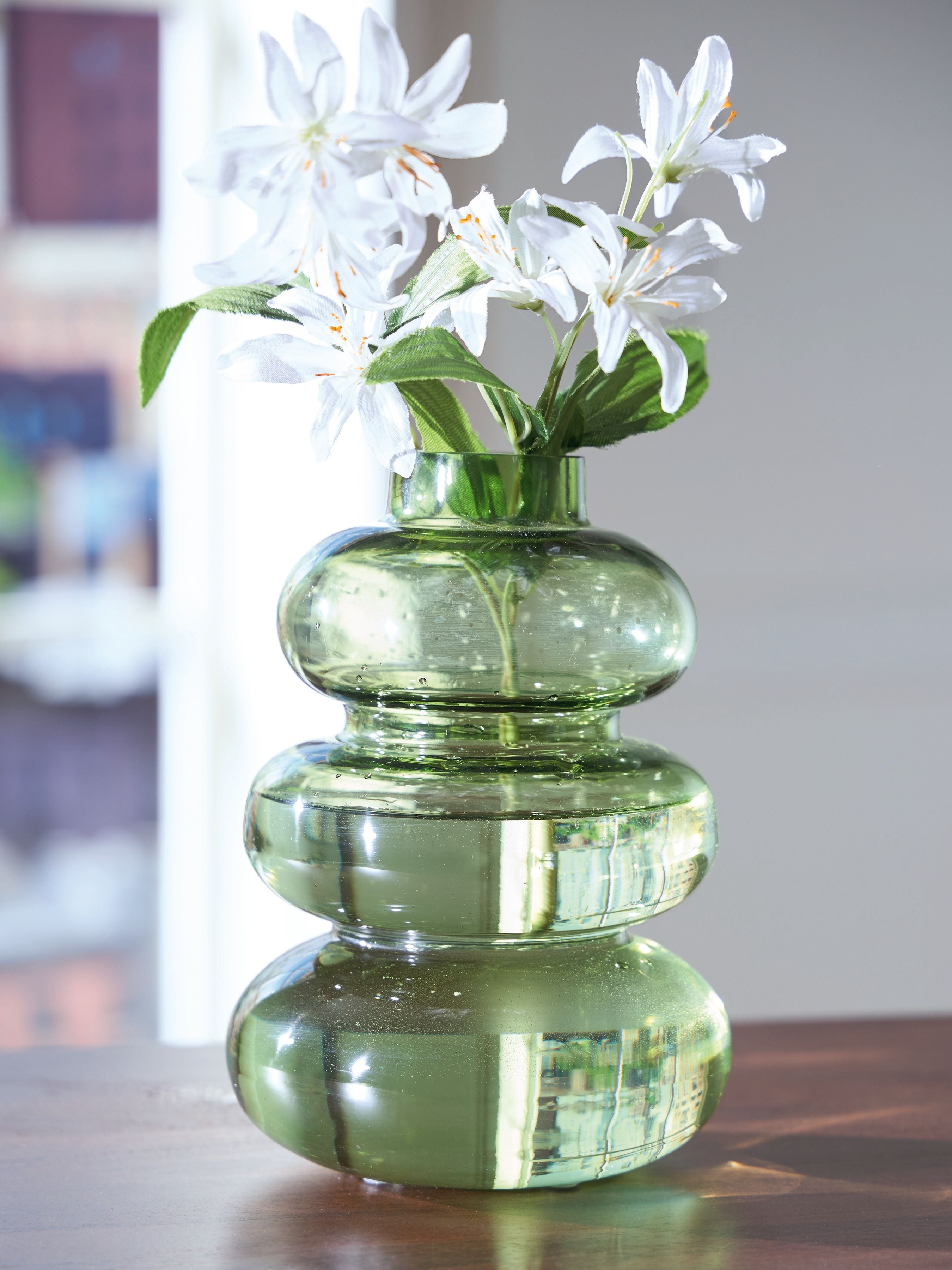 Green glass stacked vase with white blossoms and leafy stems.
