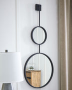 Wall-mounted stacked oval mirrors with black frames, reflecting interior objects.