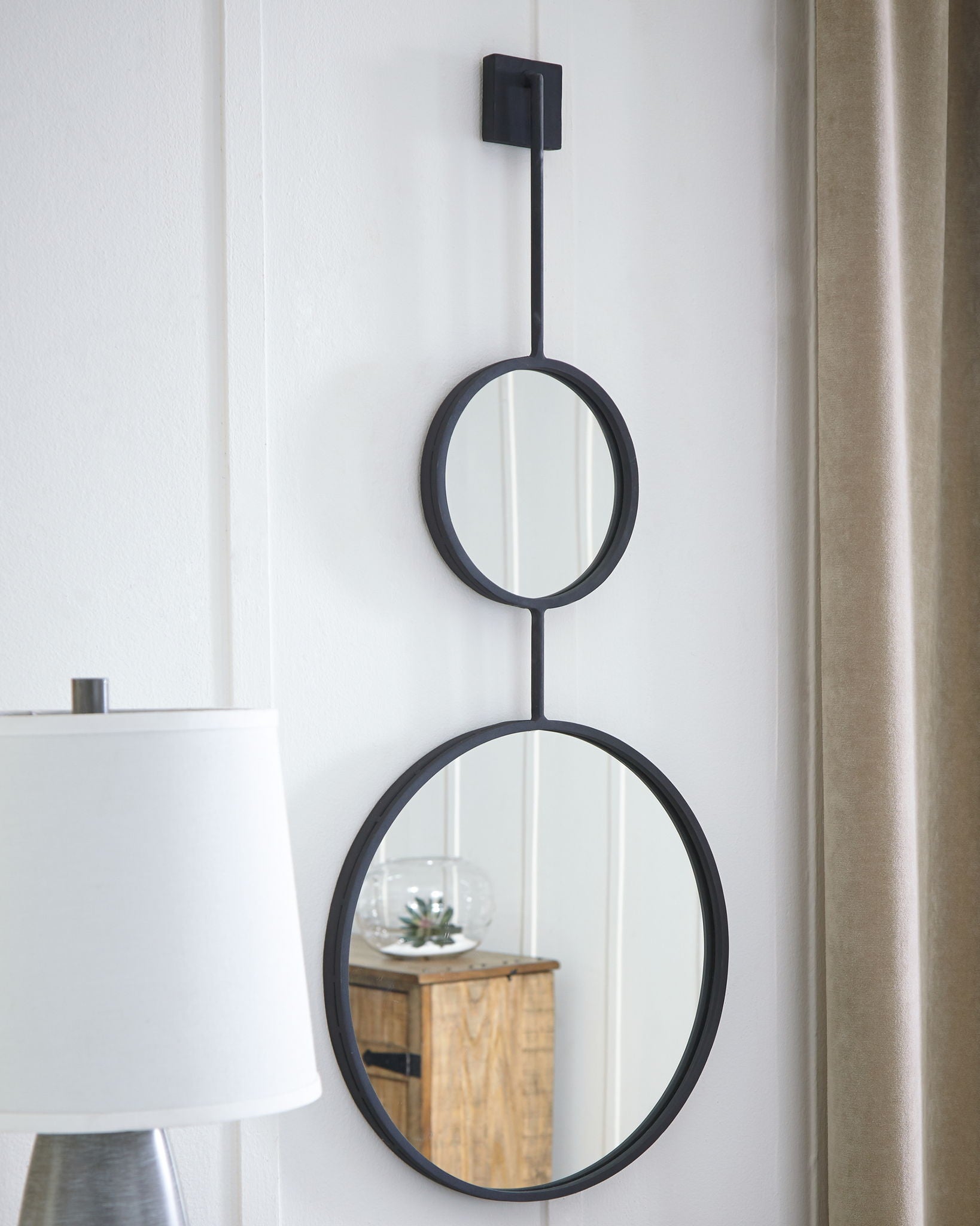 Wall-mounted stacked oval mirrors with black frames, reflecting interior objects.