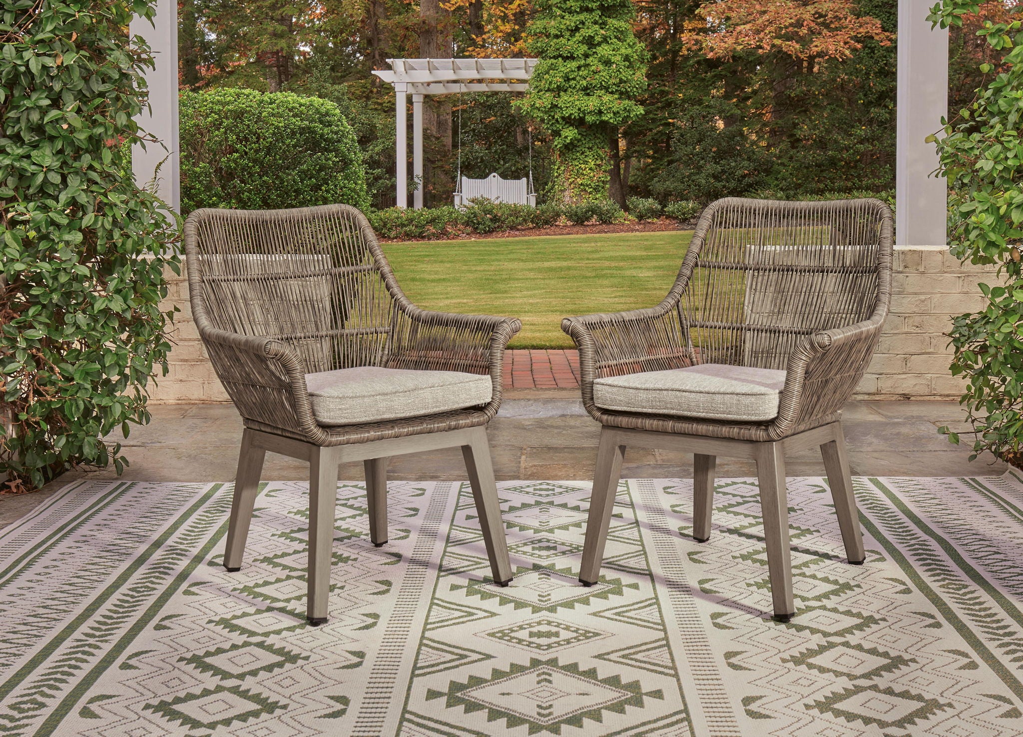 Two beige wicker armchairs with gray cushions and open slatted backs, armrests