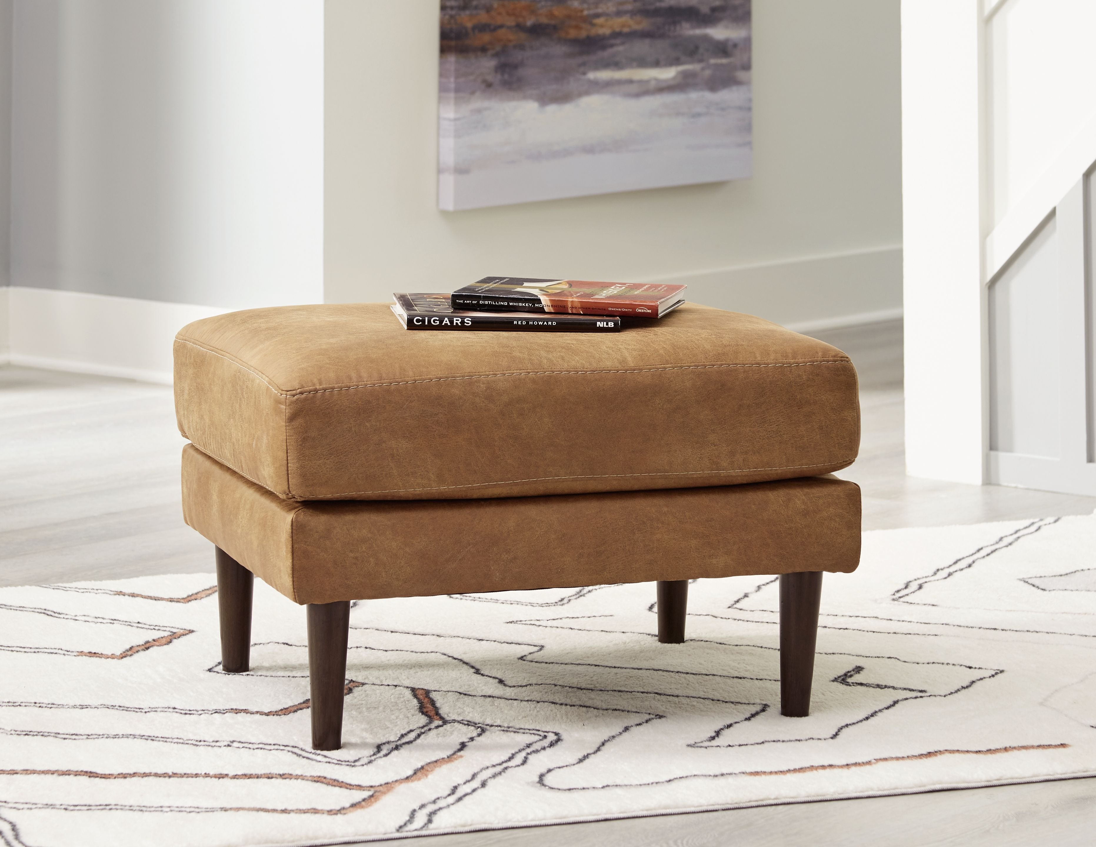 Caramel upholstered ottoman with tufted seat and dark wooden legs, front view