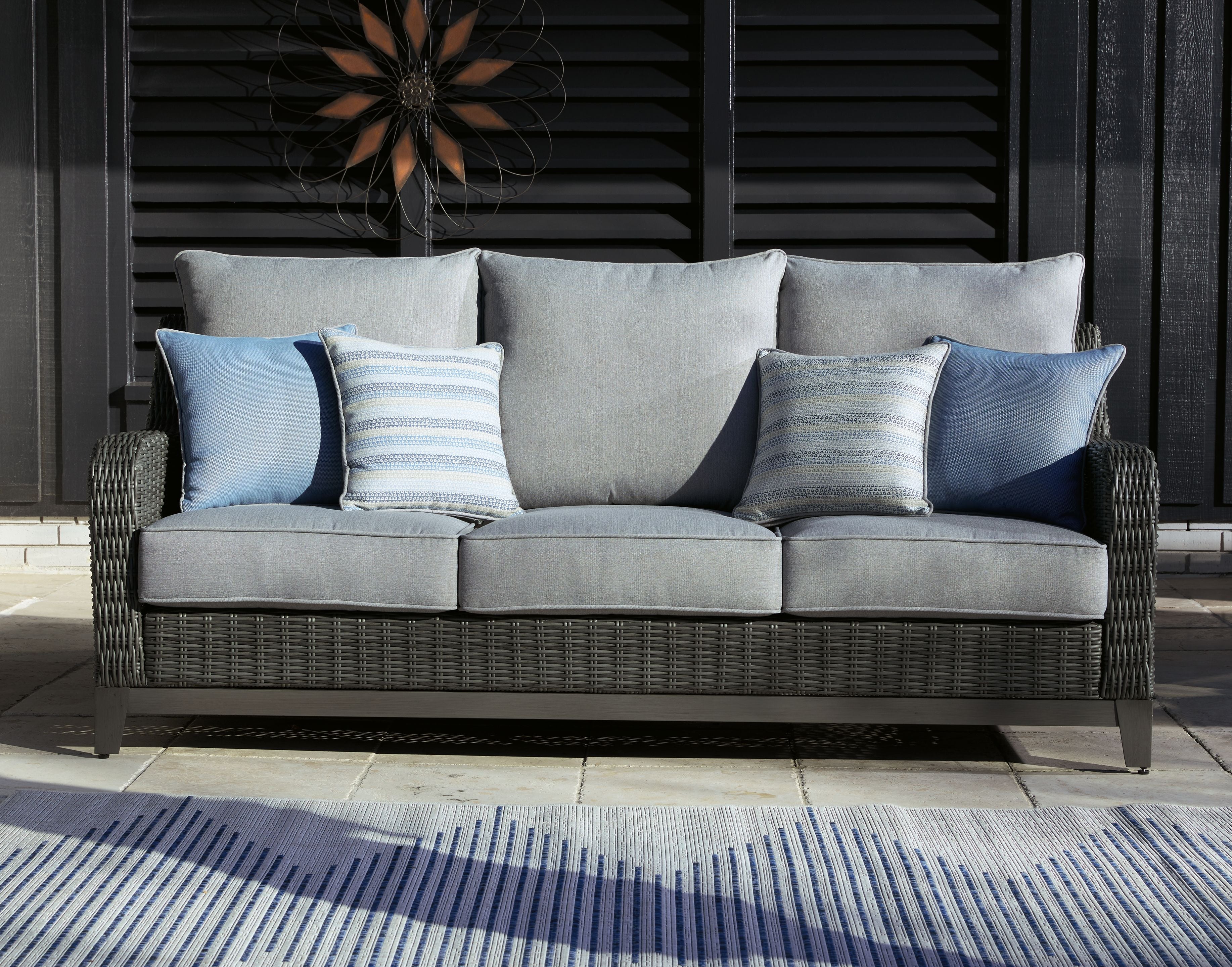 Gray woven outdoor sofa with gray back cushions and light blue striped pillows