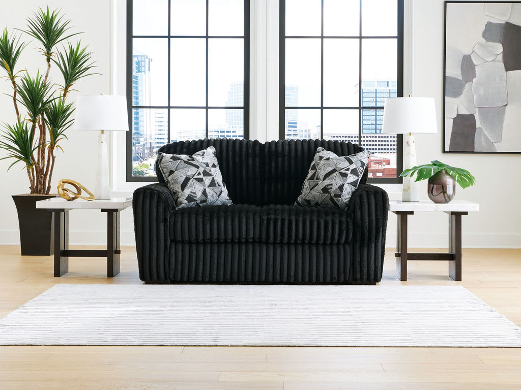 Black corduroy loveseat with tufted back, armrests, and patterned throw pillows
