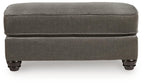 Gray fabric ottoman footstool with rounded edges and dark wood legs.