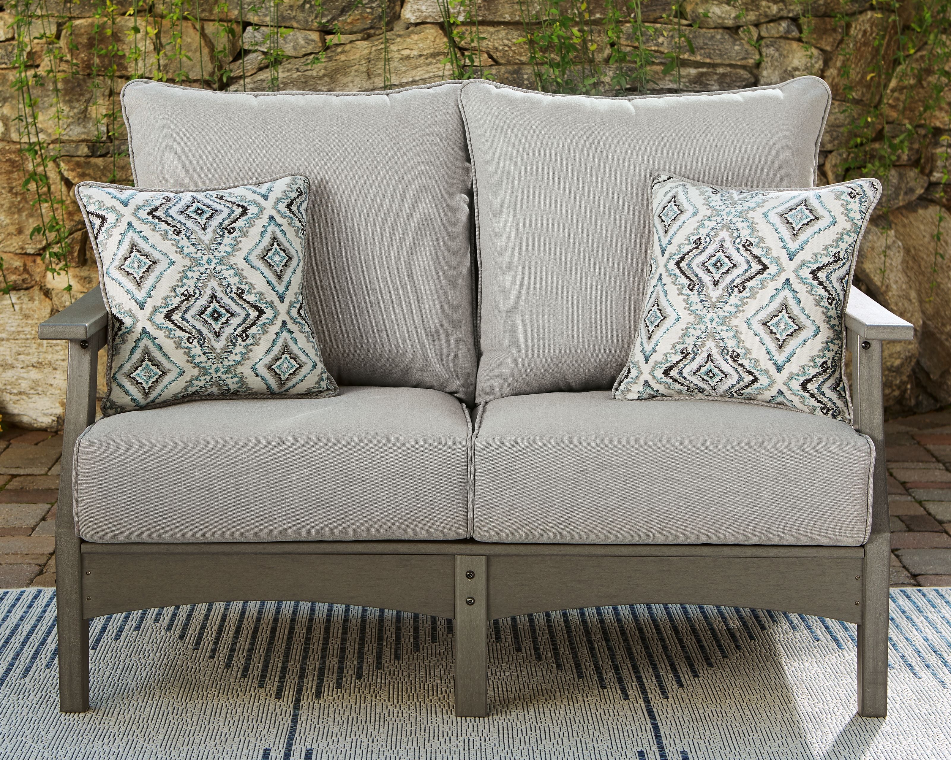 Gray loveseat with two diamond-pattern throw pillows, cushioned seat, and straight arms.