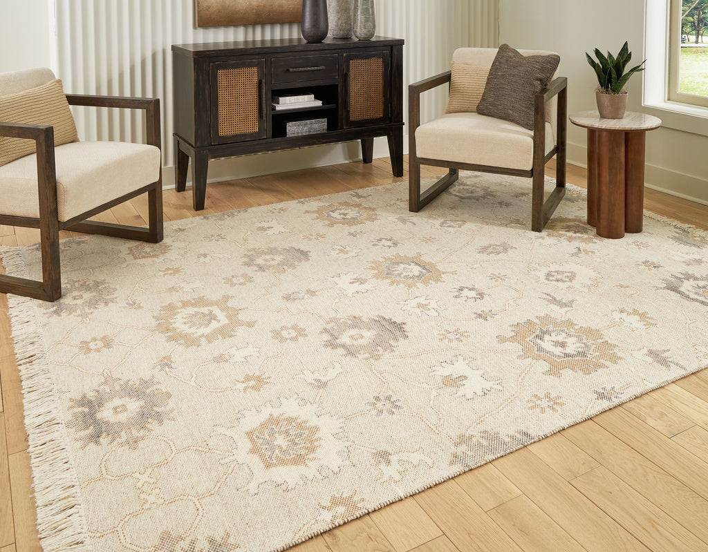 Beige rug with ornate pattern and fringed border laid on wood flooring