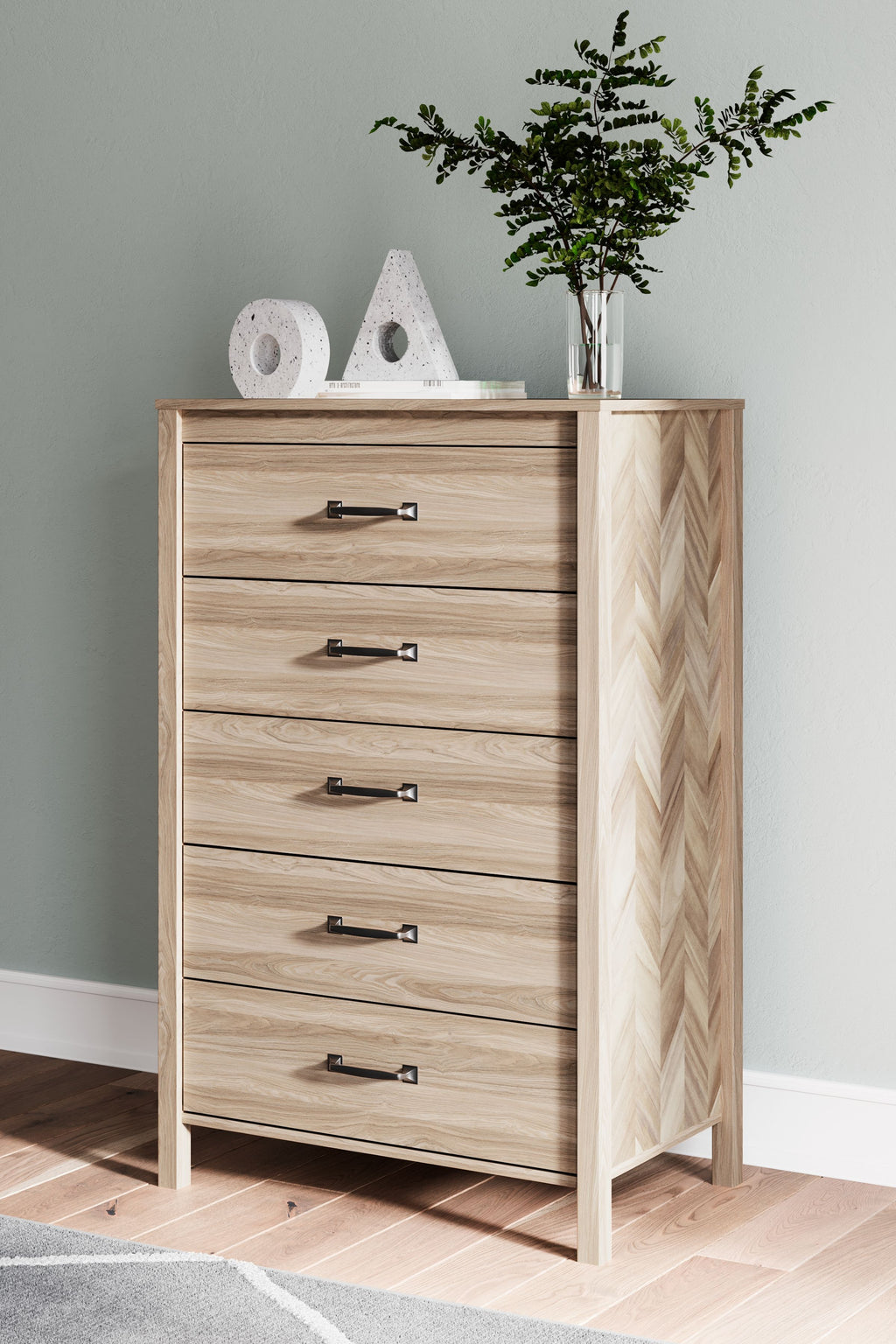 Tan five-drawer chest with black bar handles and chevron end panel