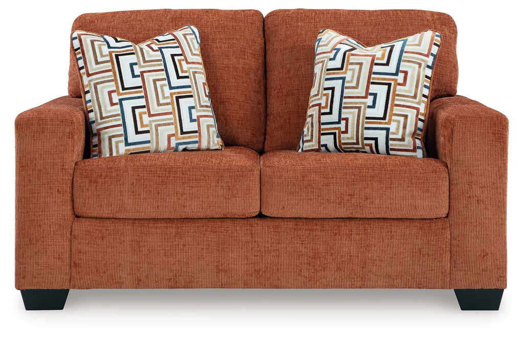 Rust orange loveseat with two patterned throw pillows on the back cushions.