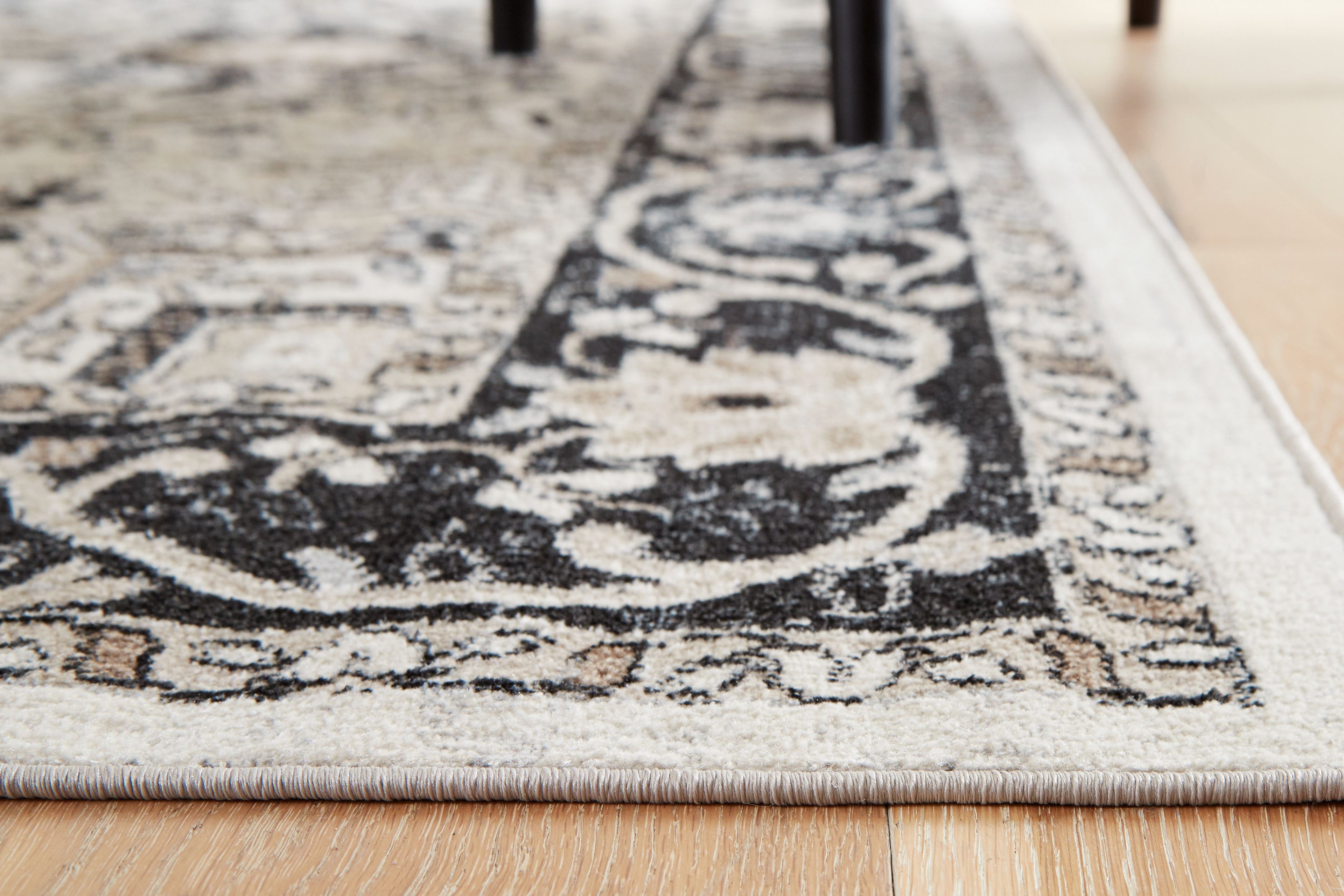 Area rug corner detail: cream and light gray field with black scrolling motif border