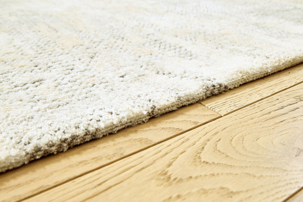 Close-up of cream rug edge with gray speckled pile and textured binding
