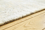 Close-up of cream rug edge with gray speckled pile and textured binding