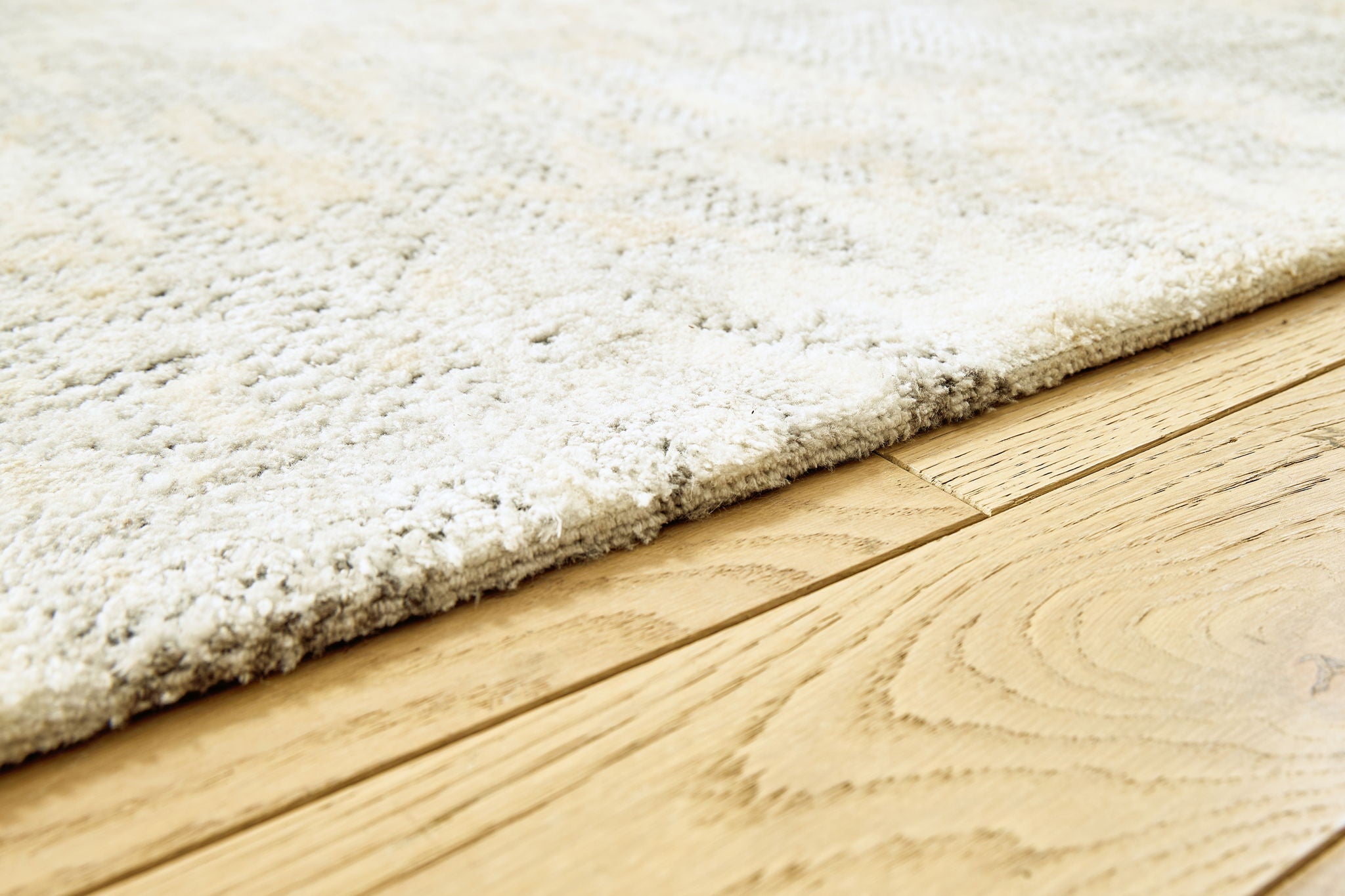 Close-up of cream rug edge with gray speckled pile and textured binding