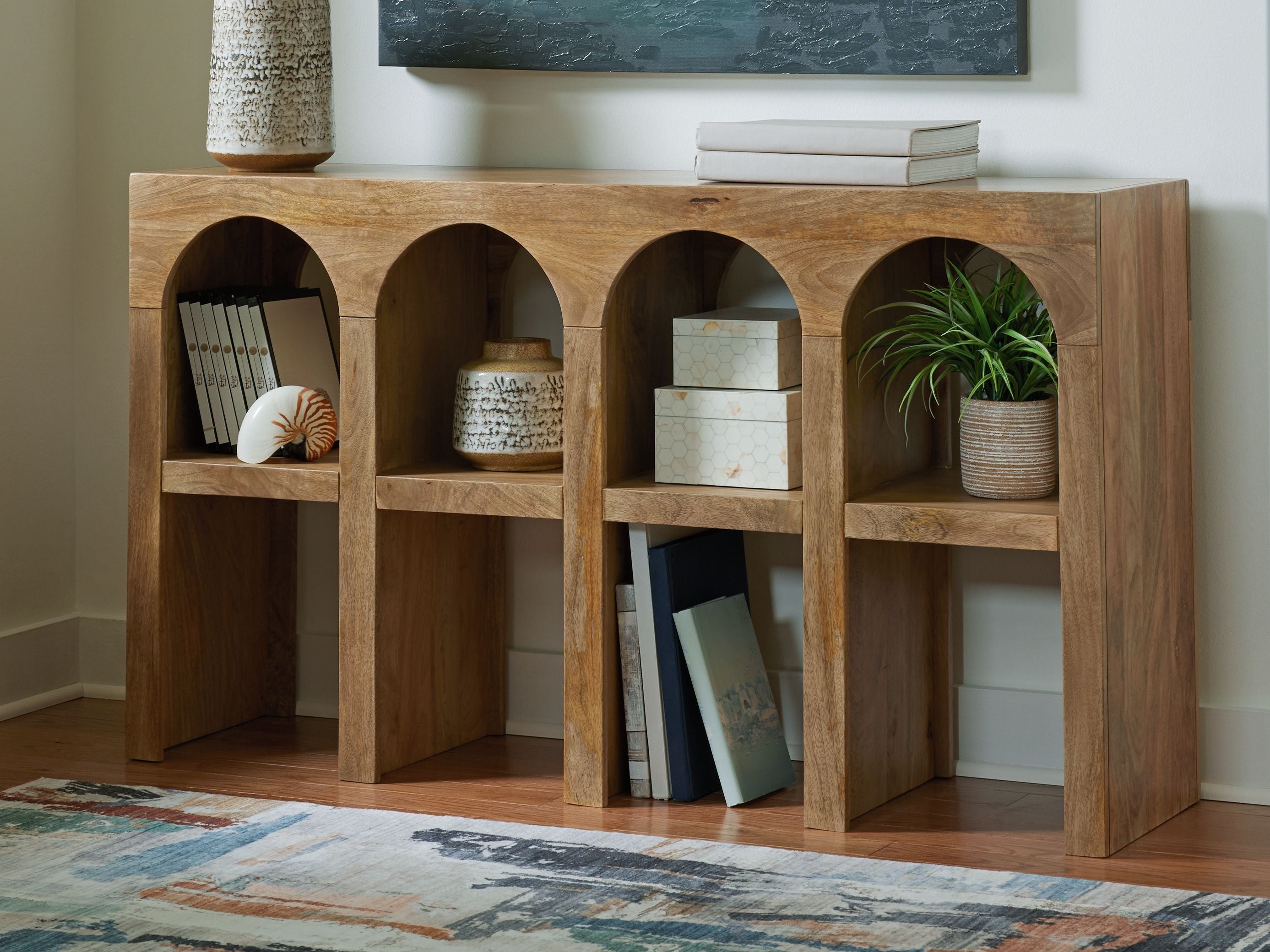 Natural brown wooden console sofa table with four arched compartments, styled with decor