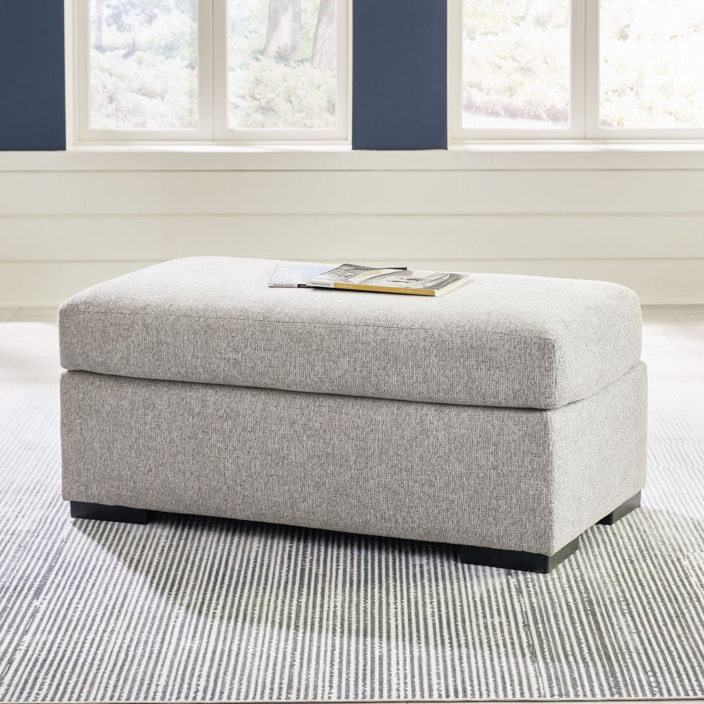 Light gray upholstered ottoman with hinged lid and dark legs