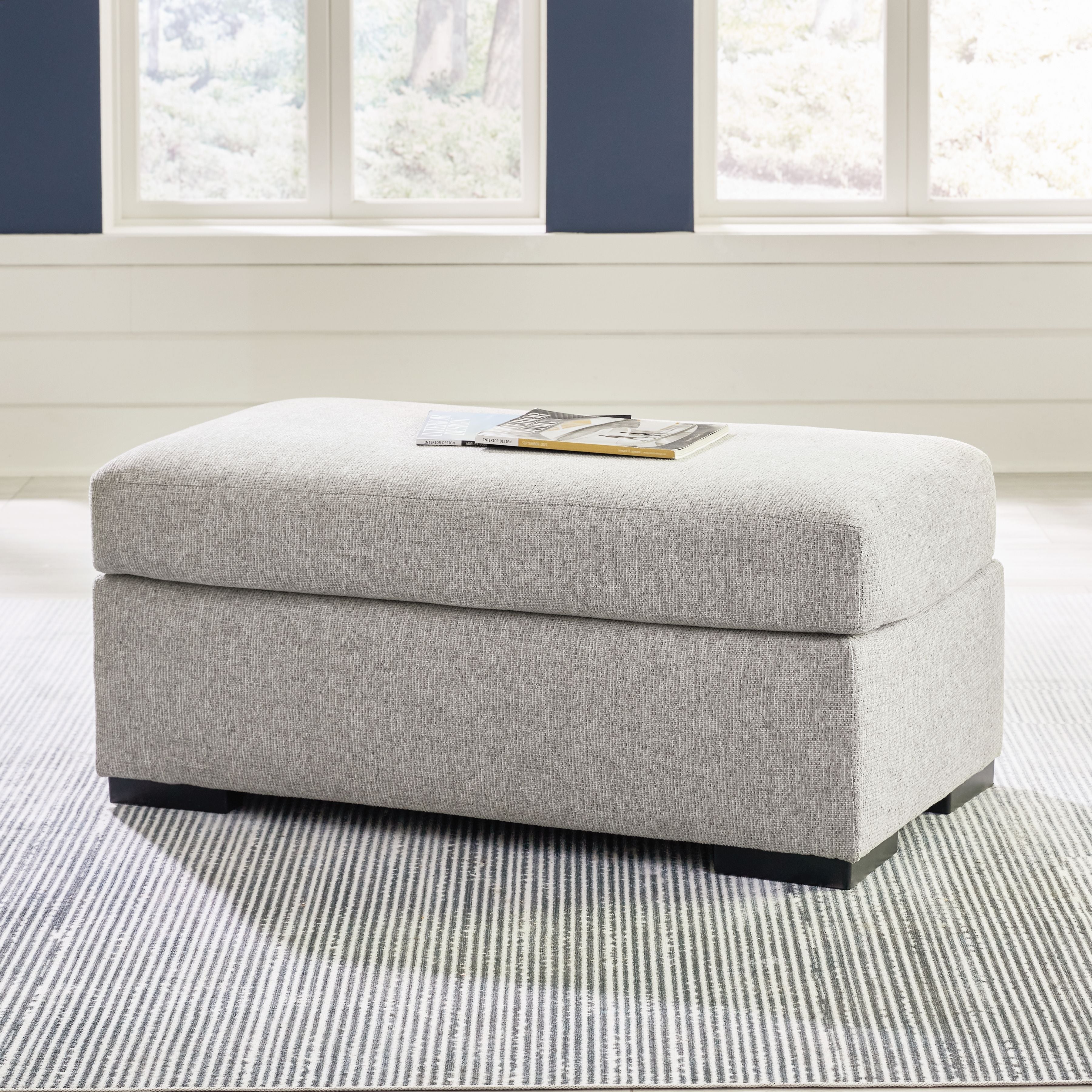Light gray upholstered ottoman with hinged lid and dark legs