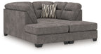 Dark gray sectional sofa chaise with tufted seat cushions and two striped accent pillows on back