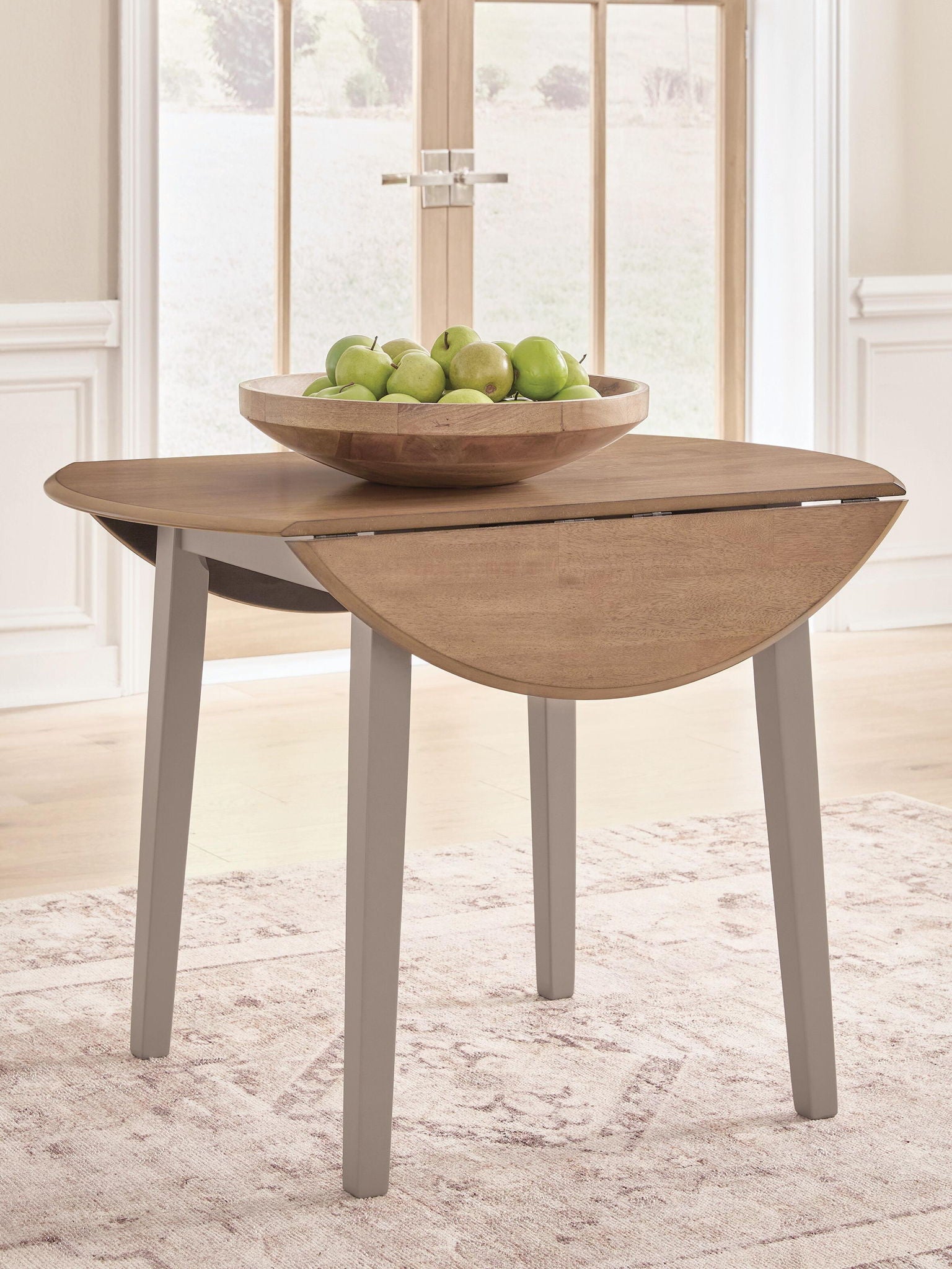 Round drop-leaf dining table with natural wood top and gray legs, leaf partially down