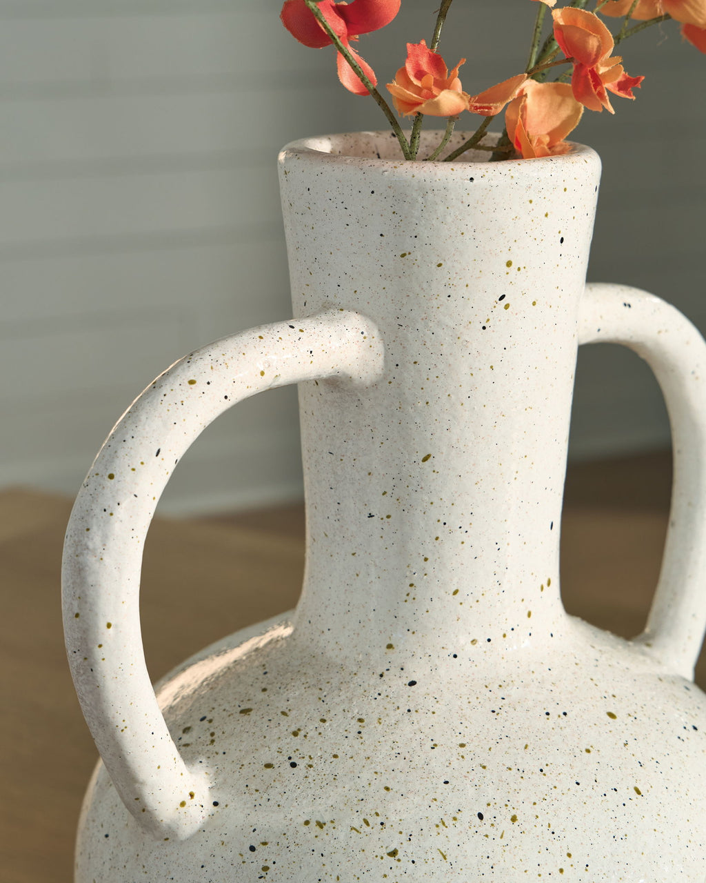 Speckled white ceramic vase with red flowers and two loop handles.